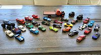 Top-down view of 32 diecast cars and trucks displayed on a wooden surface with sunlight casting shadows.