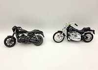 Two Maisto diecast Harley Davidson motorcycle models side by side on a white background, showing the overall size and style differences between the 2015 Street 750 (black matte) and 1984 FXST Softail (chrome and black).