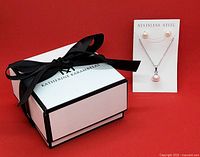Jewelry box with black ribbon and necklace/earrings on card in front on red background