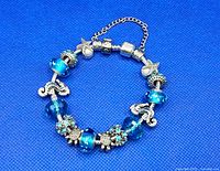 Front view of silvertone ocean themed charm bracelet on blue background