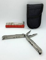 Multi tool unfolded displaying pliers, knife blade, and one screwdriver head, with set of red-handled bits and black carrying case closed beside it.