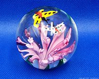 Front angle view of round clear glass paperweight with a pink flower and two butterflies inside