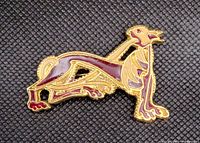 Photo showing goldtone and cherry enamel dog brooch on dark textured background.