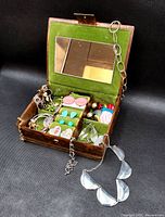 Full open vintage jewelry box showing green velvet interior, mirror, and assortment of costume jewelry items in compartments and drawer.