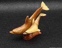 Front and side view of the wooden mother and baby dolphin sculpture on a black background, showing wood grain and detail.