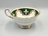 Side view of the vintage Paragon Boy Scouts commemorative teacup showing green and white fleur-de-lis design with gold gilt accents.