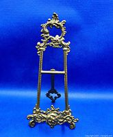 Front view of vintage solid brass ornate display easel standing upright against blue background.