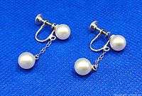Pair of vintage sterling silver double pearl dangle earrings shown flat on blue background, highlighting the screw-back closure and two pearls on each earring connected by a chain.