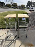 Front view of two rolling racks with wood tops and metal shelves on wheels, showing overall condition and design.
