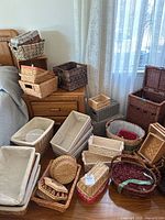 Wide view of assortment of baskets on floor and side table including multiple wicker, macrame, and woven baskets with fabric linings.