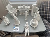 View of all 8 figurines including children in winter attire, Santa Claus, fireplace mantel, and grandfather clock on table.