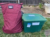 Photo of large red bag and green plastic bin labeled for Halloween blow-ups on grass outdoors.