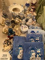Overview of collection including multiple Lenox snowman ceramic figurines, blue snowman-themed towels, soap dispensers shaped like snowmen, and various small decorations.