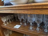 Wine goblets, dessert, champagne and cordial glasses arranged on wooden shelf, clear crystal with diamond-cut pattern and stems.
