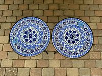 Top view of two round mosaic side tables showing detailed blue glass tile patterns and metal frames.
