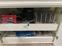 Open cabinet showing Calphalon and Emeril pots, Emerging boxed Rapid Rice cooker, and various kitchen items