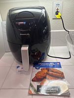 Full view of black PowerXL air fryer with manual booklet in front on counter.