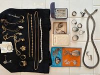 Overview of assorted gold and silver necklaces, rings, bracelets, pendants displayed on black cloth and tile