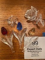 Photo showing five Swarovski crystal flower figurines on a wooden surface: red, blue, yellow stemmed flowers, clear crystal rose, smaller clear flower with heart-shaped petals.