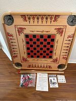 Top view of Carrom board with accessories including striker sticks, playing pieces in a plastic bag, instruction sheets, and scoring cards arranged below.