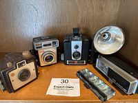 Photo of three vintage Kodak cameras including the Brownie Hawkeye, Brownie Starmatic and small box camera with brown bakelite body, also shows two vintage flash units.