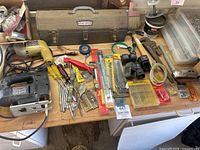 Overview of vintage tools on wooden table including electric drill, jigsaw, drill bits, hand tools, and tool box