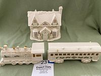 Porcelain Toy Shoppe house and Christmas village train locomotive and passenger car with holly and gold accents on a green cloth background.