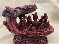 Full view of the deep reddish-brown wood sculpture showcasing the eight carved figures arranged with a naturalistic wave-like base and leafy top.