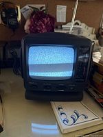 Front view of the 5-inch black and white television showing static on the screen, control knobs, and antenna.