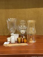 Photo of large glass hurricanes, several votive holders, and silverplate candle holders displayed on wood surface.