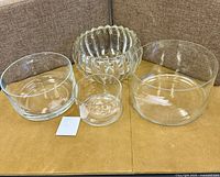 Five glass bowls on table, including plain clear, ribbed, and etched designs