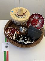 Collection on round woven tray showing miniature sombreros, straw container, pottery animal figurines, pottery bowl, mini molcajete, and small basket.