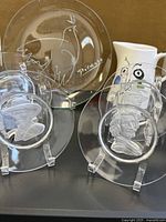 Photo showing the set of crystal and glass plates with relief portraits and the Picasso Dove plate on stands.