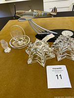 Overview of the lot with the WWII Spitfire airplane model prominently displayed behind Lalique crystal star sculptures and smaller glass figures on a gold surface.