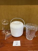 Photo of three items: clear acrylic wine holder with hand painted letter B, white plastic ice bucket with handle and fitted lid, and clear crystal cut pattern pitcher.