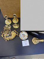 Lot arranged displaying two brass candlesticks, floral porcelain ashtray, brass hand door knocker, brass hand dish, and inkwell stand.