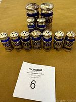 Eleven vintage William Adams salt and pepper shakers arranged in a group on a brown surface showing varying sizes and silver plated tops and lattice designs over cobalt blue glass.