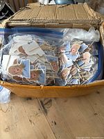 Box with plastic bags containing numerous paper cupcake toppers featuring cartoon illustrations of Taylor Swift's face. The toppers have wooden sticks attached for placing on cupcakes.