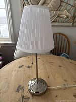 Front view of classic table lamp with white pleated fabric shade and polished metal base on wooden table.