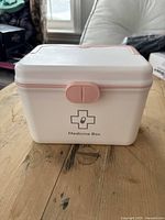 Closed white and peachy pink plastic medicine box with latch and medical cross symbol on front