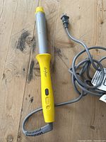 Drybar curling wand full view showing yellow handle, controls, power cord, and plug on wooden surface