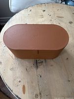 Closed oval brown leather Dyson Airwrap storage box placed on a wooden surface.