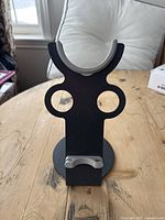 Front view of black Dyson hairdryer stand with grey padded top, circular holes on sides, and small clips at bottom for holding attachments.