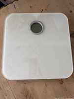 Top view showing white square bathroom scale with circular digital display in center and glossy surface.