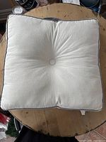 White square floor pillow on a wooden surface, showing the button tuft and grey piping.