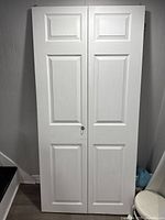 Full view of the white folding door standing upright against a wall, showing the two-panel fold design.