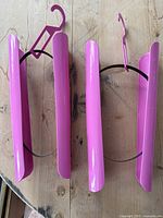 Two pink plastic boot holders on a wooden floor, showing their curved shape and black elastic connection.