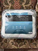 Front view of the mattress pad in its packaging showing the label with product details and brand.