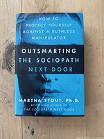 Front cover of the book 'Outsmarting the Sociopath Next Door' showing title, author, and a blue-tinted face image with some edge wear.