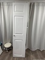 Single white folding door leaning against a curtain backdrop showing three panel design and dark knob.